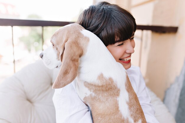 Portrait of amazing girl laughing, while embracing beagle dog looking away