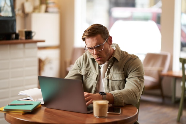 Portrait of angry man in glasses looking frustrated and typing something on laptop staring at screen