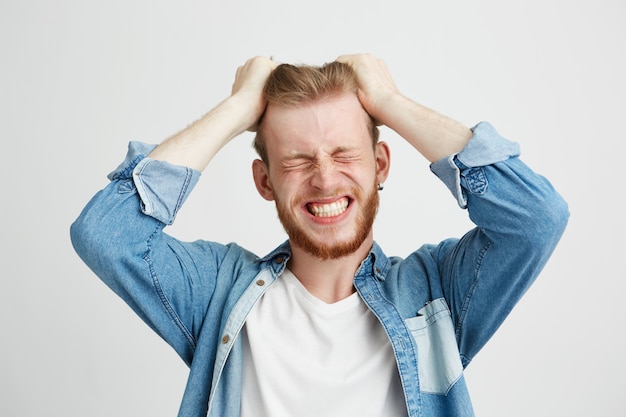 Free photo portrait of angry rage young man touching his hair clenched teeth over wite background. closed eyes.