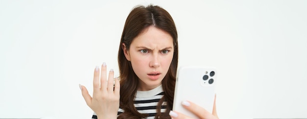 Free photo portrait of annoyed girl staring at her mobile phone screen with frustrated face white background