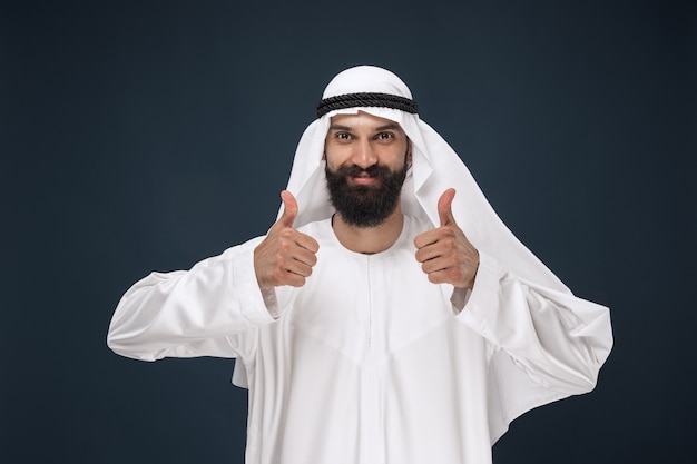 Portrait of arabian saudi businessman. Young male model standing a showing a gesture of a thumb up. Concept of business, finance, facial expression, human emotions.