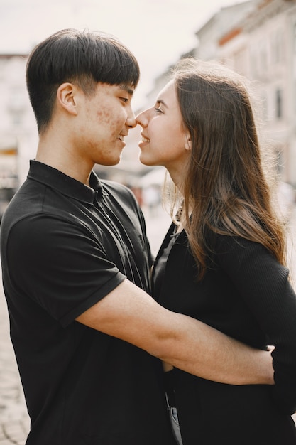 Free photo portrait of an asian boy and his caucasian girlfriend in casual wear standing on  street. couple is going to kiss each other while walking together in city