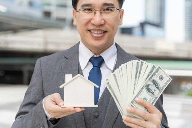 Portrait asian business man holding money us dollar bills and Model house on business district