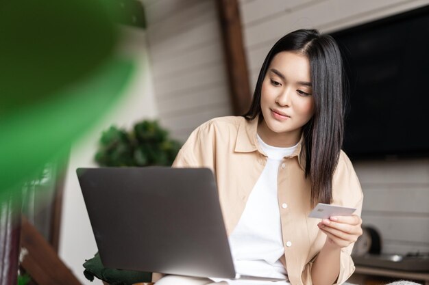 Portrait of asian girl buying on website with laptop and credit card young woman purchase online sit...