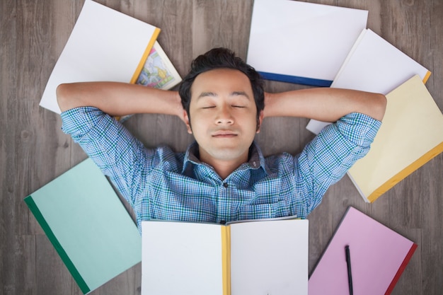 Free Photo portrait of asian man napping on floor among books