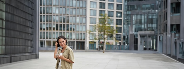 Free photo portrait of asian woman walking in city street style shot of girl with smartphone posing outdoors on