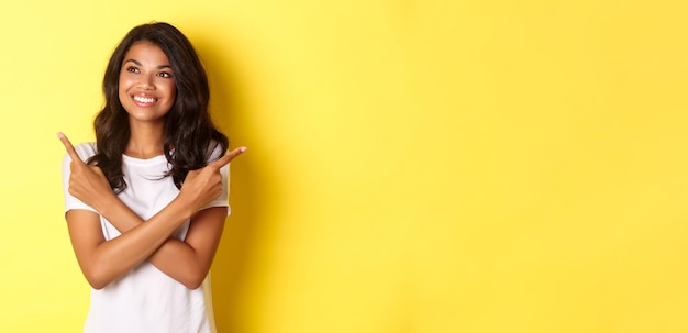 Free photo portrait of attractive africanamerican girl in white tshirt smiling and looking left pointing finger