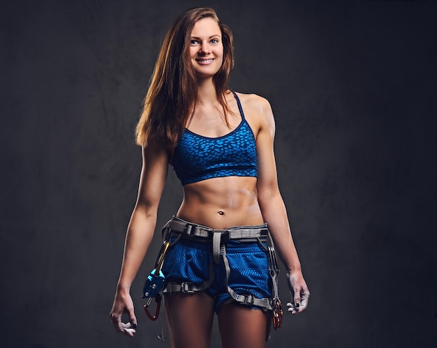 Portrait of attractive female free climber with protective gear over grey background.