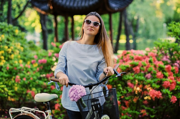 Free photo portrait of attractive female with city bicycle near traditional chinese pavilion in a park.