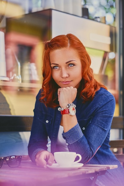 Free photo portrait of attractive redhead female drinks coffee in a cafe.