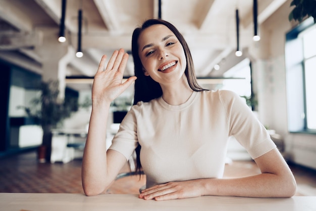 Portrait of attractive smiling businesswoman waving hand looking at camera