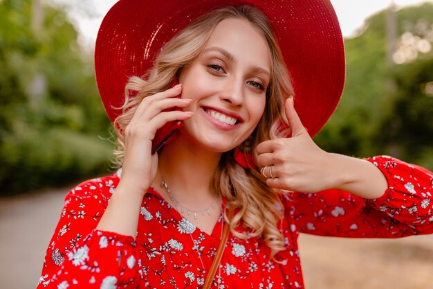 Portrait of attractive stylish blond smiling woman in straw red hat and blouse summer fashion outfit  talking on phone positive gesture emotion