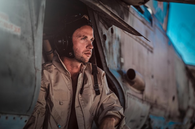 Portrait of attractive thoughful pilot outside his own fight jet. He looks away. Pilot is weaing a special helmet.