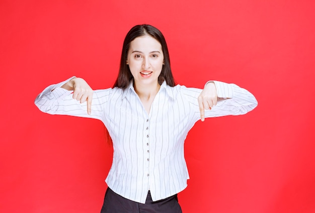 Portrait of attractive woman standing and pointing down with fingers. 