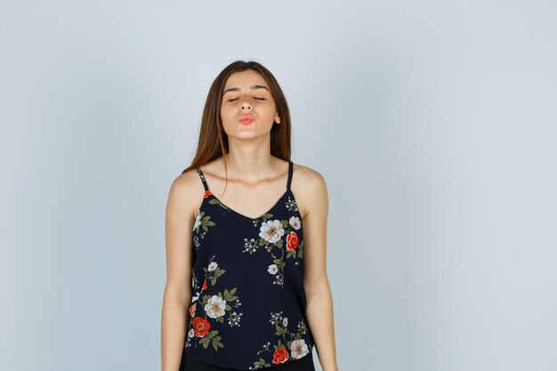 Free photo portrait of attractive young lady shutting eyes while pouting lips in blouse and looking peaceful front view