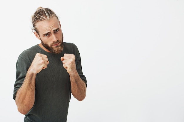 Free Photo portrait of attractive young man with trendy hairstyle and beard holding hands in front of him in boxing position going to fight.