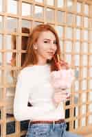 Free photo portrait of an attractive young woman holding the summer cocktail glass covered with cotton candy