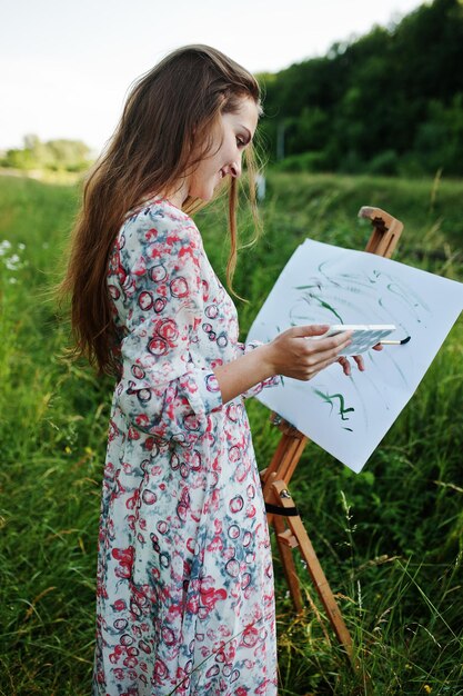 Portrait of an attractive young woman in long dress painting with watercolor in nature