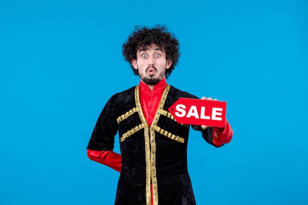 Free photo portrait of azeri man in traditional costume holding sale nameplate on blue background ethnic novruz shopping