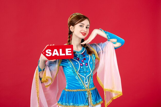 Portrait of azeri woman in traditional dress holding sale nameplate on red