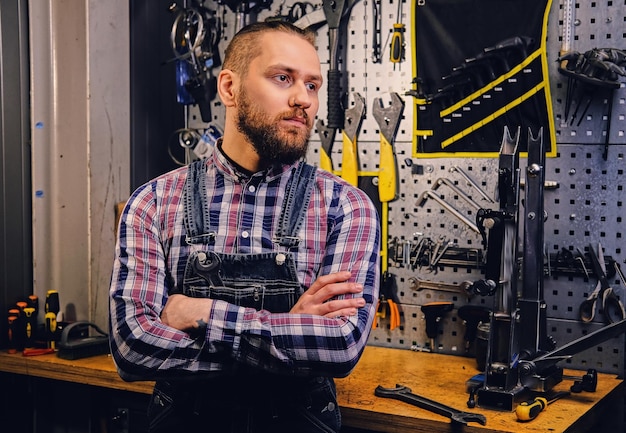 Portrait of bearded bicycle mechanic with crossed arms over tool stand background.