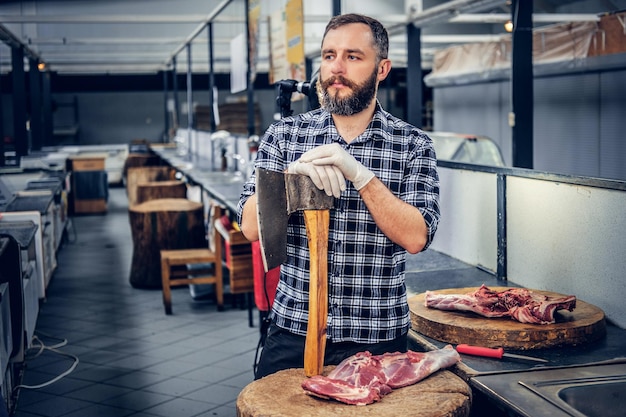 Free Photo portrait of a bearded meat man dressed in a fleece shirt holds an axe and fresh cut meat.