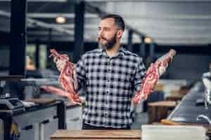 Free photo portrait of a bearded meat man dressed in a fleece shirt holds fresh cut meat in a market.