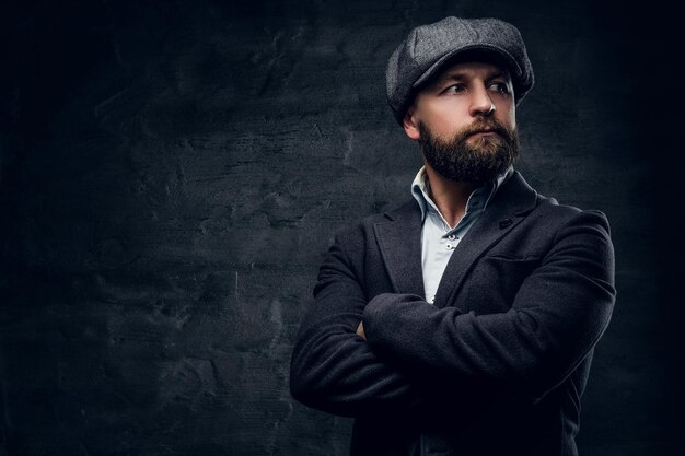 Portrait of bearded middle age male with crossed arms on a chest, dressed in a woolen suit and a tweed cap.