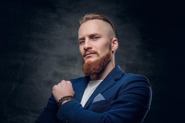 Portrait of bearded redhead hipster male dressed in a blue jacket over grey background.