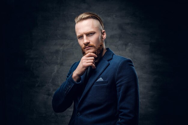 Portrait of bearded redhead hipster male dressed in a blue jacket over grey background.