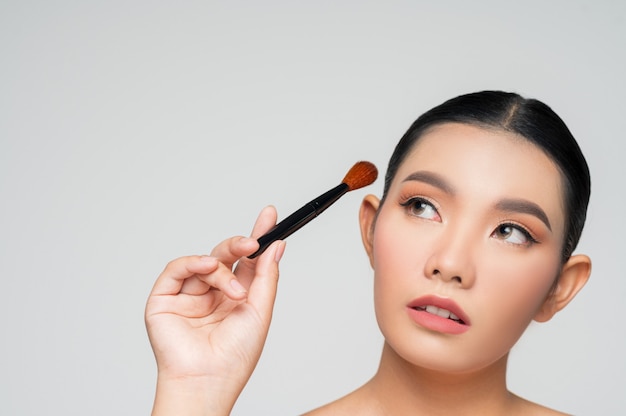 Portrait of Beautiful Asian woman holding makeup blusher brush