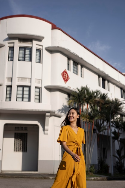 Free photo portrait of beautiful asian woman posing in the city while wearing yellow dress