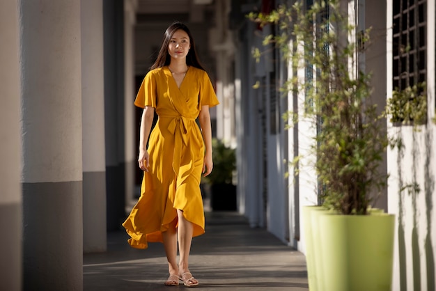 Free photo portrait of beautiful asian woman in yellow dress posing outdoors in the city