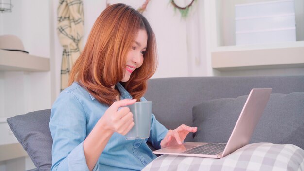 Portrait of beautiful attractive Asian woman using computer or laptop holding a warm cup of coffee