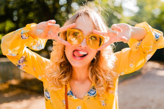 Portrait of beautiful blond stylish emotional woman in yellow blouse wearing sunglasses, funny crazy face expression