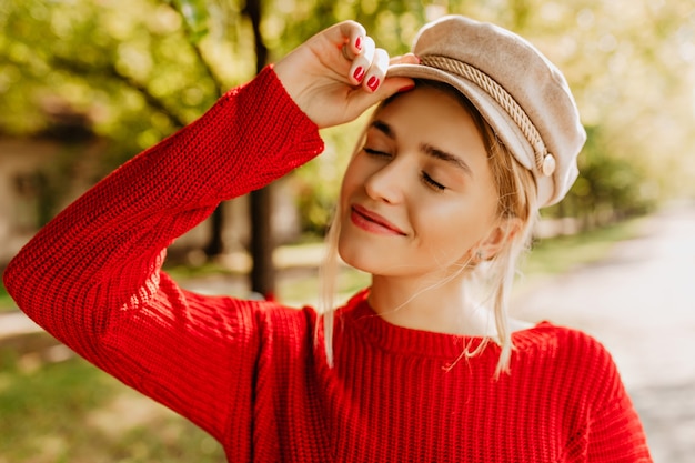 Free Photo portrait of a beautiful blonde girl in nice red sweater and light hat posing in the autumn park.