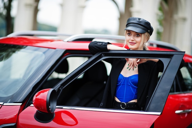 Free Photo portrait of beautiful blonde sexy fashion woman model in cap and in all black blue corset with bright makeup near red city car