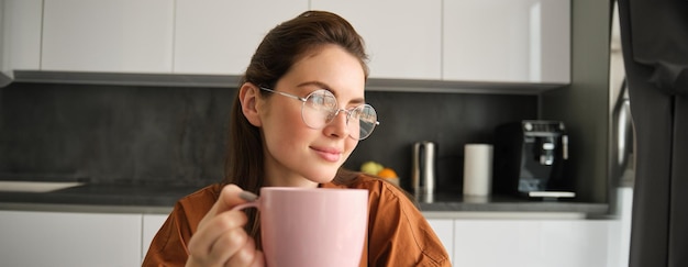 Free Photo portrait of beautiful brunette woman sitting in kitchen taking a break for cup of coffee girl drinks