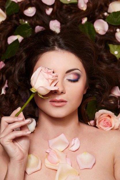 Portrait of beautiful brunette woman with long curly hair and bright makeup witjh flowers in hair