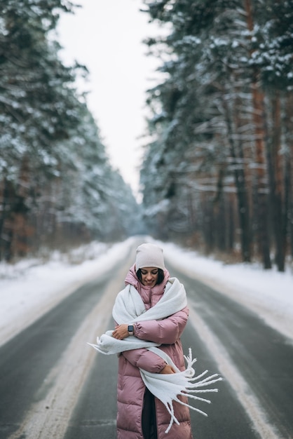 Free photo portrait of a beautiful caucasian woman on a road through snowy forest