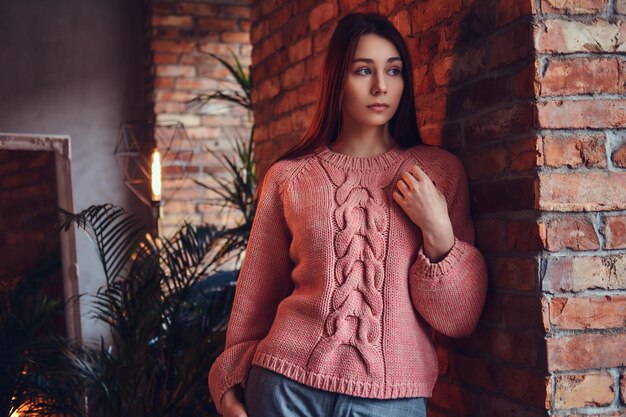 Free Photo portrait of a beautiful charming brunette dressed in stylish clothes leaning against a brick wall in a room with loft interior.