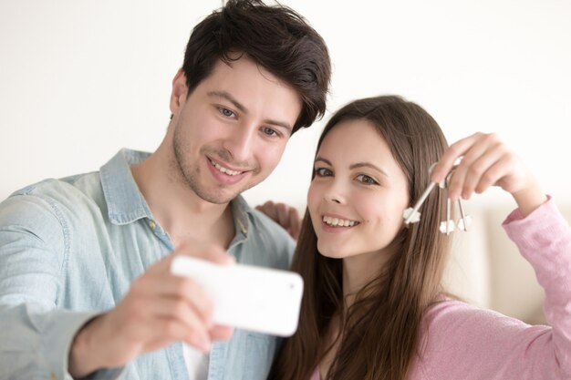 Portrait of beautiful couple making selfie on mobile holding key