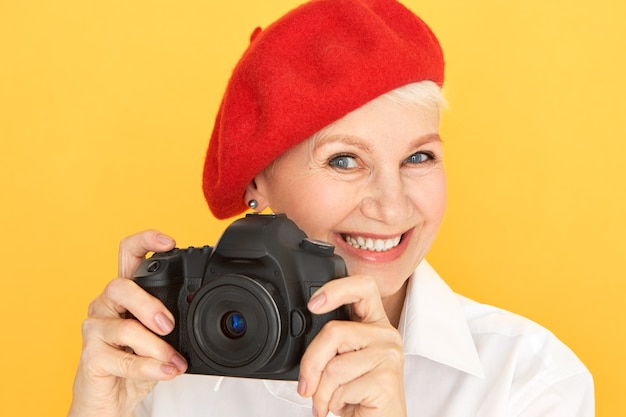 Portrait of beautiful energetic mature female photographer with short hair and wrinkles taking images using black professional camera