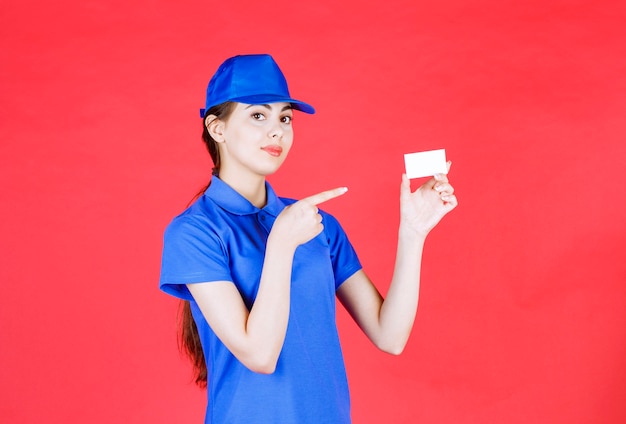 Portrait of beautiful female courier pointing empty business card on red.