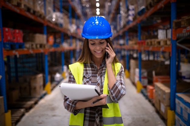 Portrait of beautiful female warehouse worker having conversation on cell phone in large storage distribution center