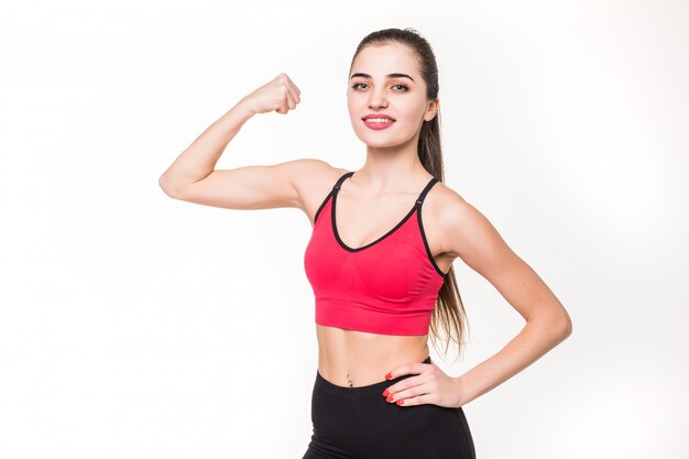 Portrait of a beautiful fitness woman showing her biceps on a white wall