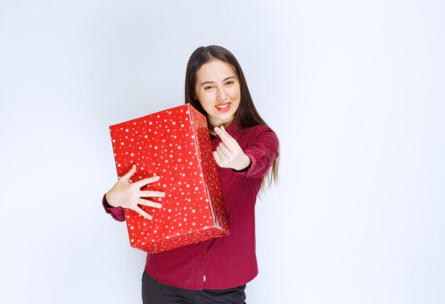 Portrait of a beautiful girl holding present box  over white wall .