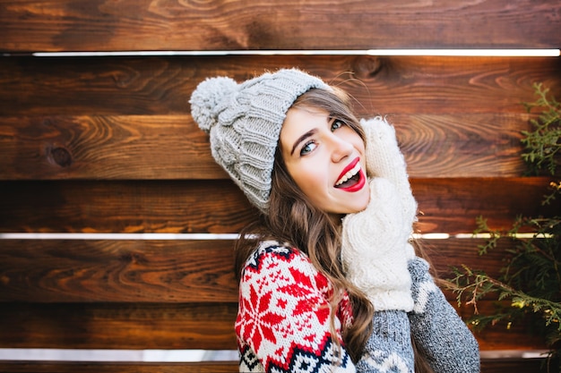 Free Photo portrait beautiful girl with long hair and red lips in knitted hat and gloves on wooden . she is smiling .