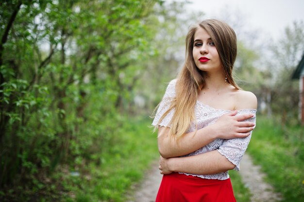 Portrait of beautiful girl with red lips at spring blossom garden wear on red dress and white blouse