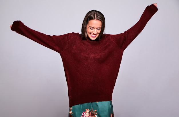 Portrait of beautiful happy cute brunette woman model in casual warm red sweater clothes isolated on gray with evening makeup and colorful lips